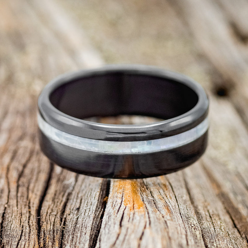 Shown here is "Vertigo", a handcrafted men's wedding ring featuring a mother of pearl inlay, laying flat.