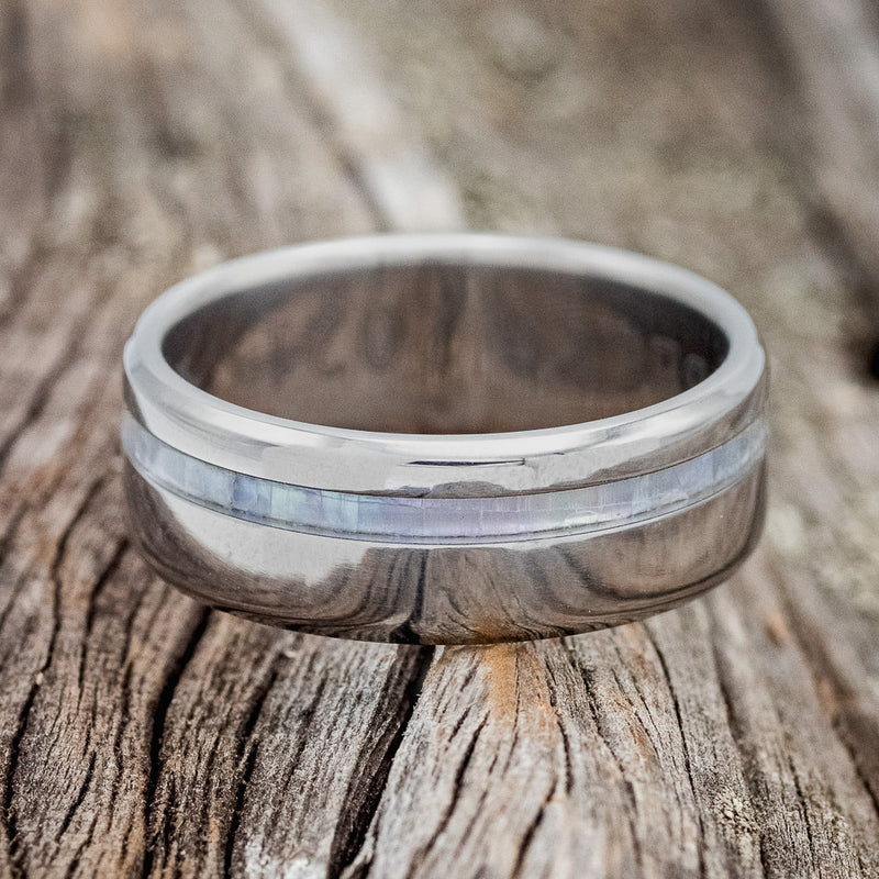 Shown here is "Vertigo", a custom, handcrafted men's wedding ring featuring a mother of pearl inlay, laying flat. Additional inlay options are available upon request.