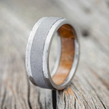 Shown here is "Sedona", a custom, handcrafted men's wedding ring featuring an authentic whiskey barrel stave oak as the lining of the ring with hammered edges and a sandblasted center piece, upright facing left. Additional inlay options are available upon request.