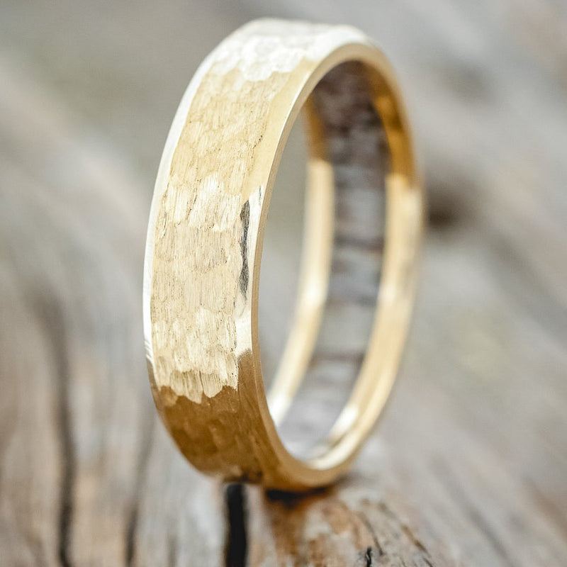 Shown here is a handcrafted men's wedding ring featuring a hammered finish and antler lining on any of our available base material options, upright facing left. Additional inlay options are available upon request.