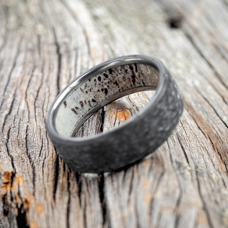 Shown here is a handcrafted men's wedding ring featuring a hammered finish and antler lining on any of our available base material options, tilted right. Additional inlay options are available upon request.