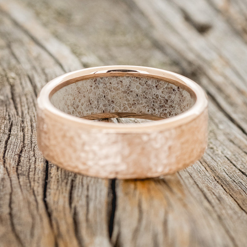 Shown here is a handcrafted men's wedding ring featuring a hammered finish and antler lining on any of our available base material options, laying flat. Additional inlay options are available upon request.