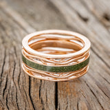 Shown here is men's "Artemis", a custom, handcrafted men's wedding ring featuring a single channel with a moss inlay, laying flat. Additional inlay options are available upon request.
