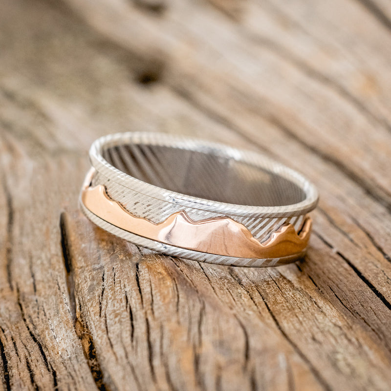 Shown here is "Revolution", a handcrafted fidget men's wedding ring featuring a free-spinning 14K rose gold mountain range on a Damascus steel band, tilted left. Additional inlay options are available upon request.