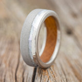 Shown here is "Vertigo", a custom, handcrafted men's wedding ring featuring whiskey barrel lining and a mother of pearl inlay, upright facing left. Half of this titanium band has a hammered finish and the other half is sandblasted. Additional inlay options are available upon request.