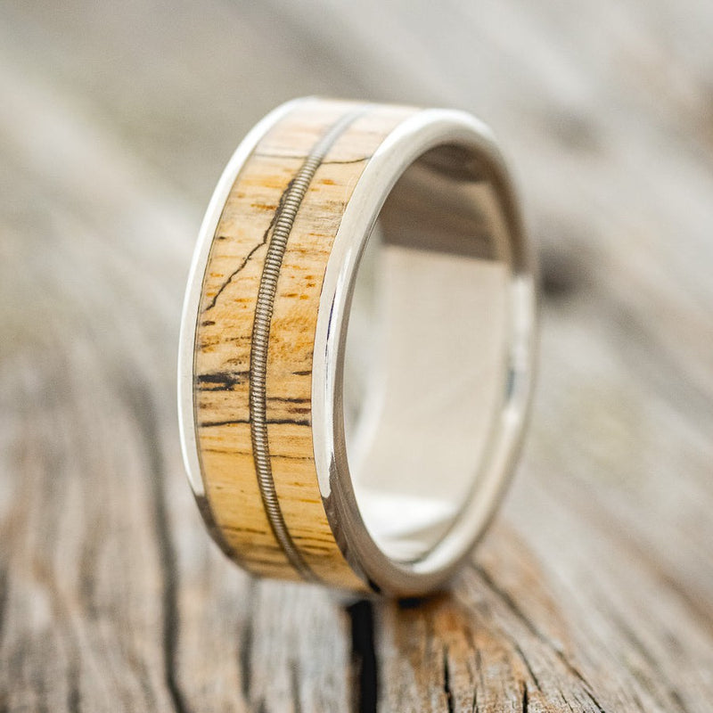 Shown here is "Rainier", a custom, handcrafted men's wedding ring featuring a single channel spalted maple wood and guitar string inlays on a titanium band, upright facing left. Additional inlay options are available upon request.