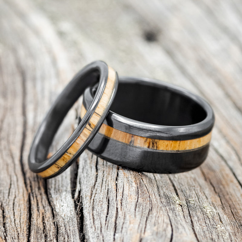 Shown here is a matching wedding band set featuring "Eterna" & "Vertigo", laying together. "Vertigo" is a handcrafted wide wedding band featuring a spalted maple wood inlay. "Eterna" is a stacking-style wedding band featuring a spalted maple wood inlay.