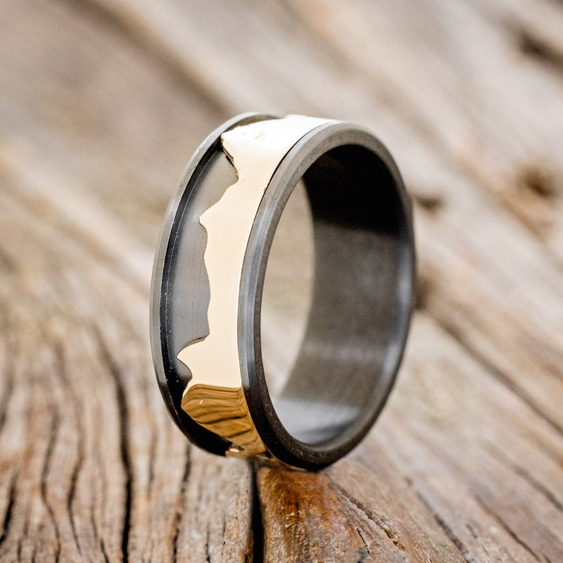 Shown here is "Revolution", a handcrafted fidget men's wedding ring featuring a free-spinning 14K yellow gold mountain range on a fire-treated black zirconium band, upright facing left. Additional inlay options are available upon request.