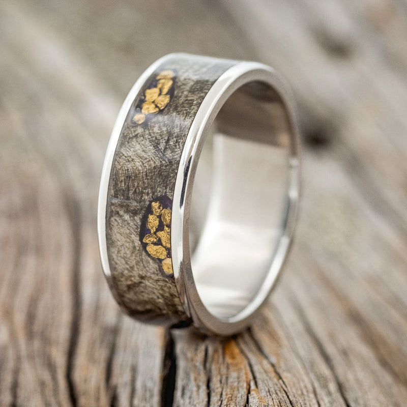 Shown here is "Rainier", a custom, handcrafted men's wedding ring featuring a buckeye burl wood channel on a titanium base with gold nuggets set in the burls, upright facing left. Additional inlay options are available upon request.