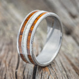 Shown here is "Rio", a custom, handcrafted men's wedding ring featuring 3 channels with ironwood and antler inlays on an etched Damascus Steel band, upright facing left. Additional inlay options are available upon request.