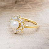 Shown here is "Dorothea", a white Akoya pearl women's engagement ring with opal and diamond accents, facing left. Many other center stone options are available upon request.