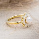 Shown here is "Dorothea", a white Akoya pearl women's engagement ring with opal and diamond accents, facing right. Many other center stone options are available upon request.