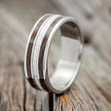 Shown here is "Rio", a custom, handcrafted men's wedding ring featuring 3 channels with ironwood and antler inlays on a titanium band, upright facing left. Additional inlay options are available upon request.