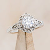 Shown here is "Eileen", a vintage-style moissanite women's engagement ring with diamond accents, on stand facing slightly right. Many other center stone options are available upon request.