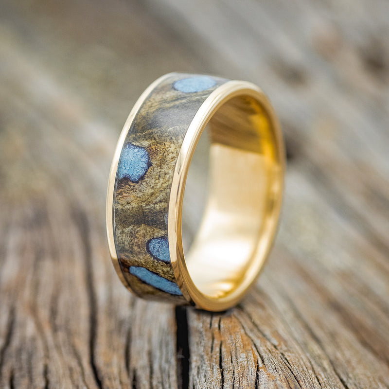 Shown here is "Rainier", a custom, handcrafted men's wedding ring featuring buckeye burl wood with hand-crushed turquoise filling the knots and burl holes, upright facing left. Additional inlay options are available upon request.