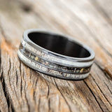 Shown here is "Rio", a custom, handcrafted men's wedding ring featuring 3 channels with antler and camo inlays on a fire-treated black zirconium band, tilted left. Additional inlay options are available upon request.