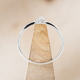 Shown here is a dainty-style knot women's stacking band with diamond accents, side view on stand.