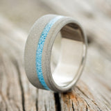 Shown here is "Vertigo", a custom, handcrafted men's wedding ring featuring a turquoise inlay with a sandblasted band, upright facing left. Additional inlay options are available upon request.