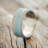 Shown here is "Vertigo", a custom, handcrafted men's wedding ring featuring a turquoise inlay with a sandblasted finish, upright facing left. 