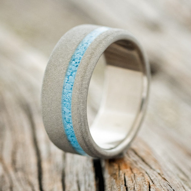 Shown here is "Vertigo", a custom, handcrafted men's wedding ring featuring a turquoise inlay with a sandblasted band, upright facing left. Additional inlay options are available upon request.