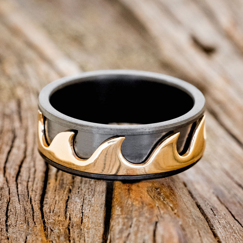 Shown here is "Revolution", a handcrafted fidget men's wedding ring featuring free-spinning 14K yellow gold waves on a fire-treated black zirconium band, laying flat. Additional inlay options are available upon request.