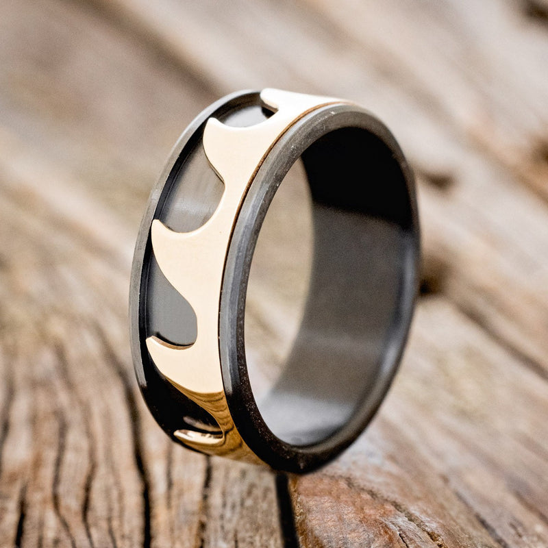 Shown here is "Revolution", a handcrafted fidget men's wedding ring featuring free-spinning 14K yellow gold waves on a fire-treated black zirconium band, upright facing left. Additional inlay options are available upon request.