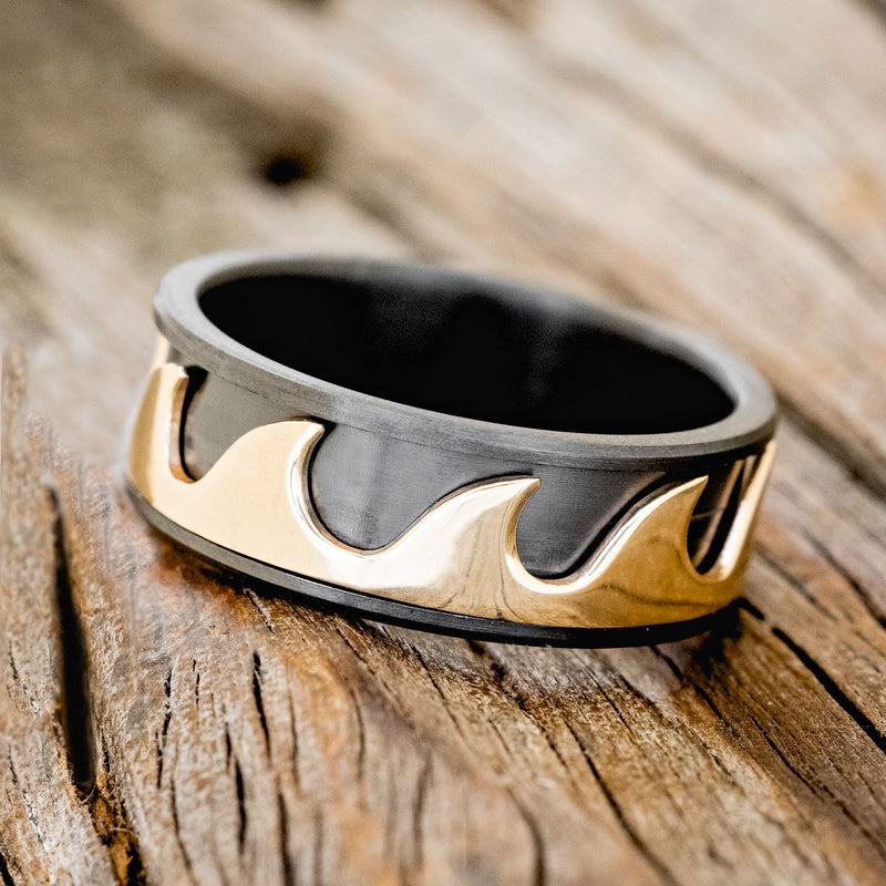 Shown here is "Revolution", a handcrafted fidget men's wedding ring featuring free-spinning 14K yellow gold waves on a fire-treated black zirconium band, tilted left. Additional inlay options are available upon request.