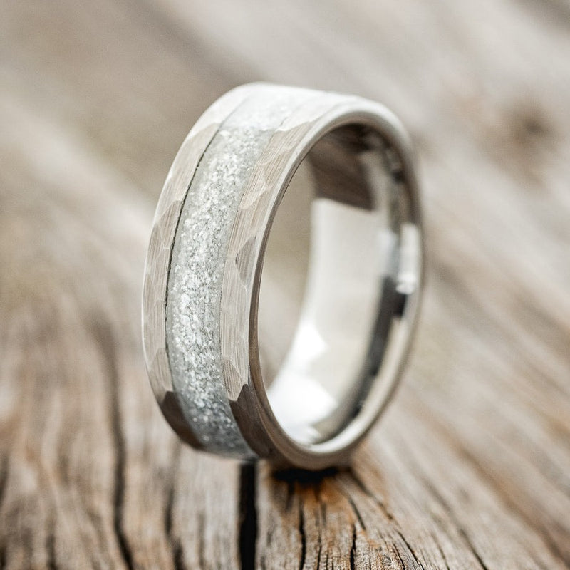 Shown here is "Apollo", a custom, handcrafted men's wedding ring featuring a tungsten band with faceted edges, upright facing left. The inlay is called Diamond dust, which is a unique blend of materials that allows for a beautiful shine of color. Additional inlay options are available upon request.