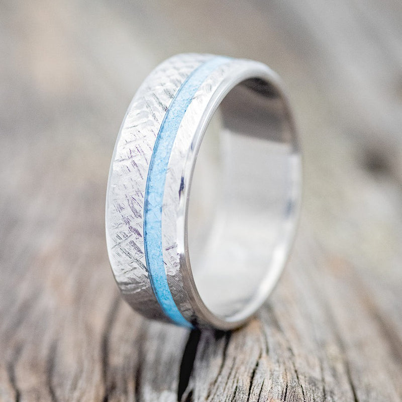 Shown here is "Vertigo", a custom, handcrafted men's wedding ring featuring a turquoise inlay with a crosshatched finish, upright facing left. Additional inlay options are available upon request.