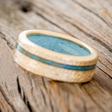 Shown here is "Vertigo", a custom, handcrafted men's wedding ring featuring an offset copper patina inlay and a turquoise lining on a hammered 14K gold band, tilted left. Additional inlay options are available upon request.