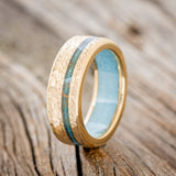 Shown here is "Vertigo", a custom, handcrafted men's wedding ring featuring an offset copper patina inlay and a turquoise lining on a hammered 14K gold band, upright facing left. Additional inlay options are available upon request.