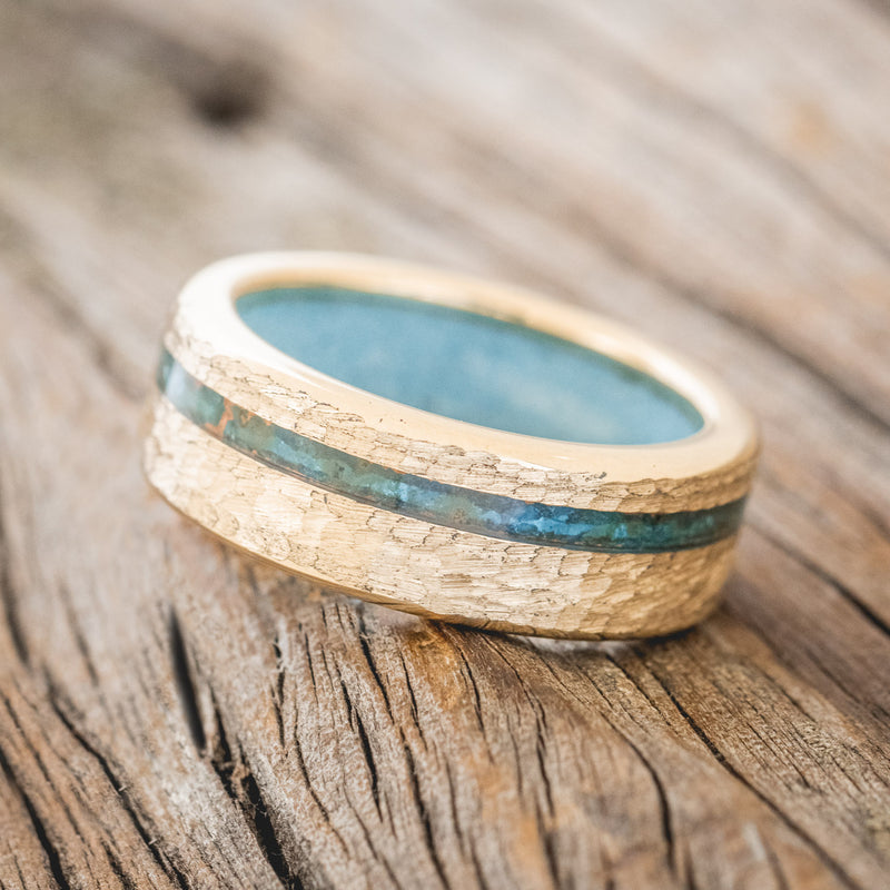 Shown here is "Vertigo", a custom, handcrafted men's wedding ring featuring an offset copper patina inlay and a turquoise lining on a hammered 14K gold band, tilted left. Additional inlay options are available upon request.