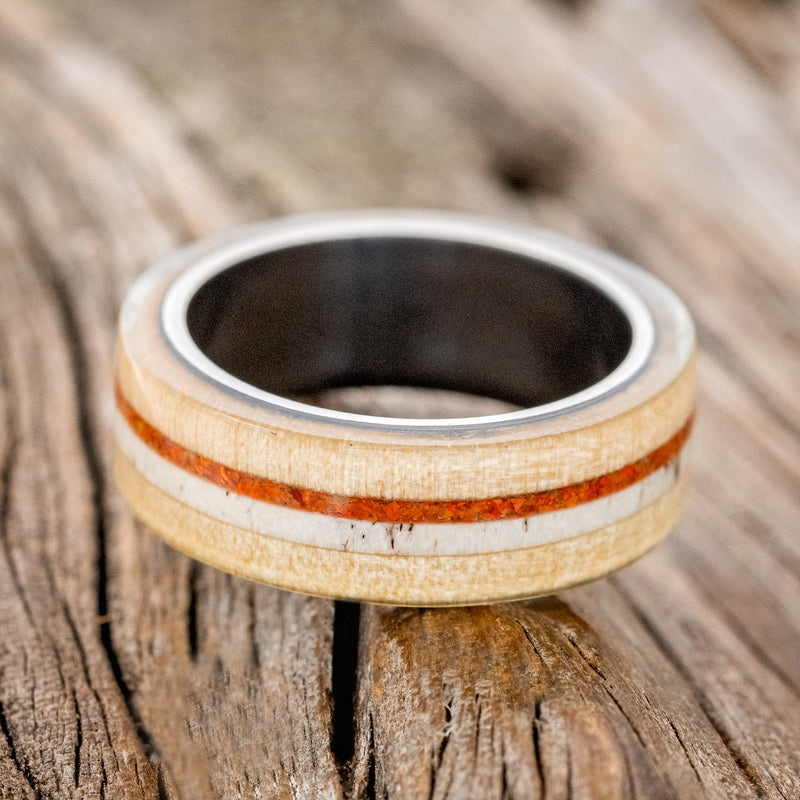 Shown here is "Canyon", a custom, handcrafted men's wedding ring featuring an aspen wood overlay with antler and orange opal inlays, laying flat. Additional inlay options are available upon request.
