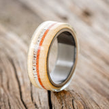 Shown here is "Canyon", a custom, handcrafted men's wedding ring featuring an aspen wood overlay with antler and orange opal inlays, upright facing left. Additional inlay options are available upon request.