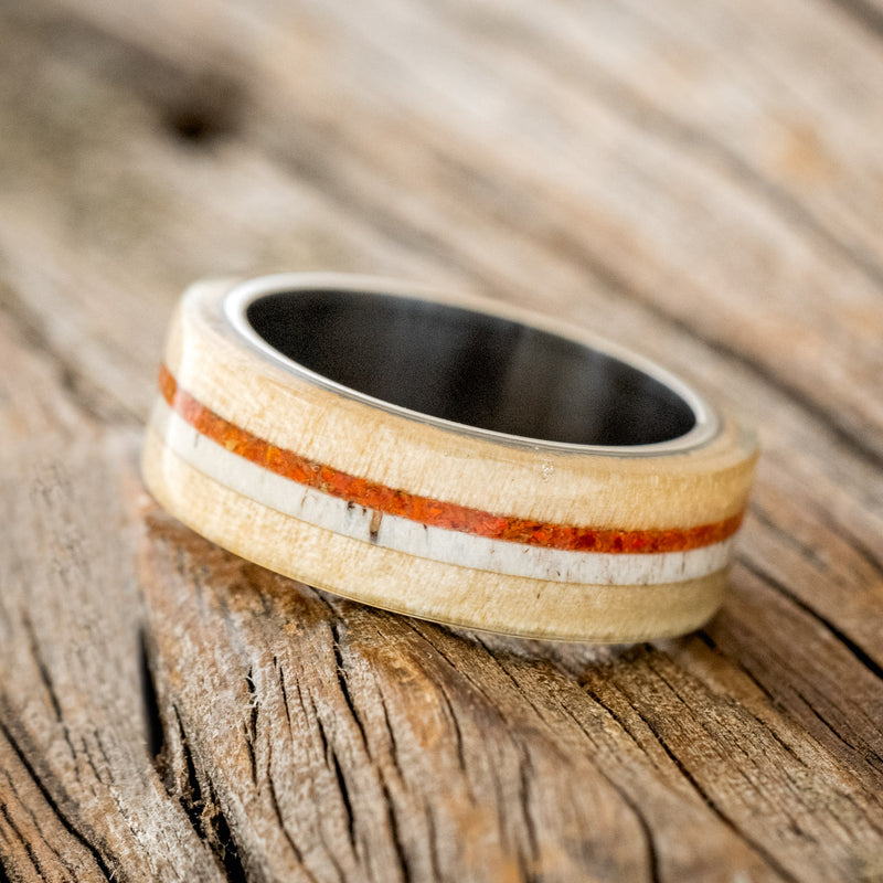 Shown here is "Canyon", a custom, handcrafted men's wedding ring featuring an aspen wood overlay with antler and orange opal inlays, tilted left. Additional inlay options are available upon request.