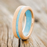 Shown here is "Vertigo", a custom, handcrafted men's wedding ring featuring a turquoise lining, with an offset turquoise inlay, shown here on a 14K gold band, upright facing left. Additional inlay options are available upon request.