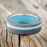 Shown here is "Vertigo", a custom, handcrafted men's wedding ring featuring a turquoise lining, with an offset turquoise inlay on a sandblasted band, laying flat. Additional inlay options are available upon request.