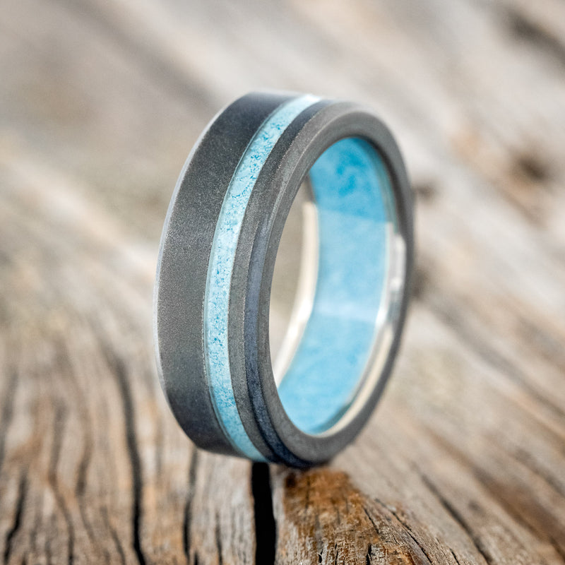 Shown here is "Vertigo", a custom, handcrafted men's wedding ring featuring a turquoise lining, with an offset turquoise inlay on a sandblasted band, upright facing left. Additional inlay options are available upon request.