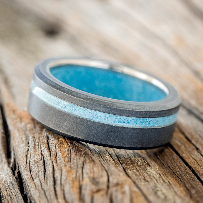 Shown here is "Vertigo", a custom, handcrafted men's wedding ring featuring a turquoise lining, with an offset turquoise inlay on a sandblasted band, tilted left. Additional inlay options are available upon request.