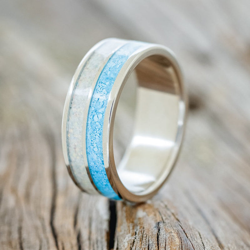 Shown here is "Dyad", a custom, handcrafted men's wedding ring featuring 2 channels with fire and ice opal and turquoise inlays, upright facing left. Additional inlay options are available upon request.