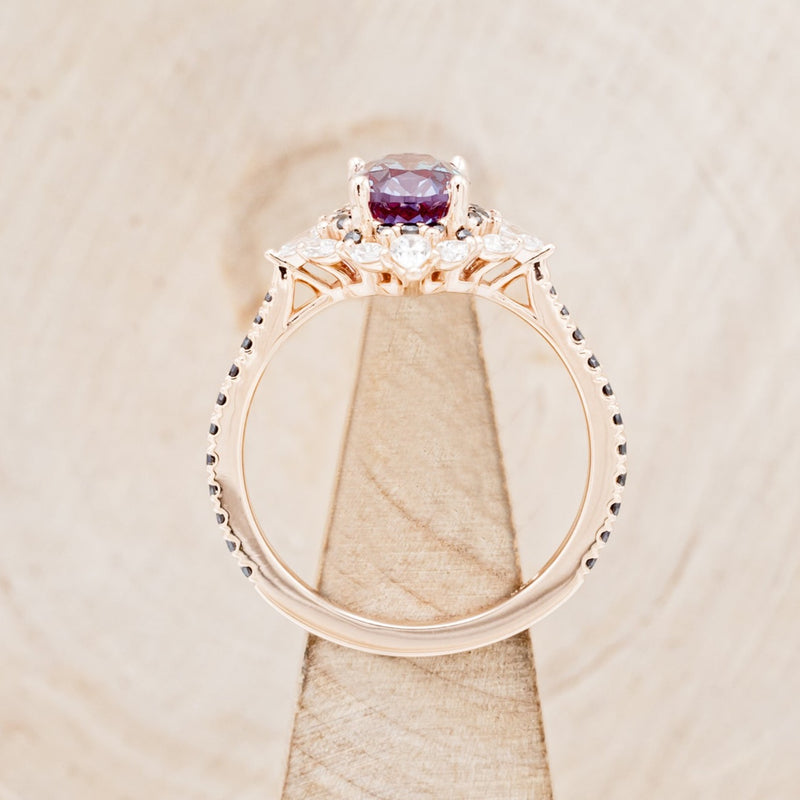 Shown here is "North Star", an oval lab-created alexandrite women's engagement ring with a diamond halo and black diamond accents, side view on stand. Many other center stone options are available upon request.