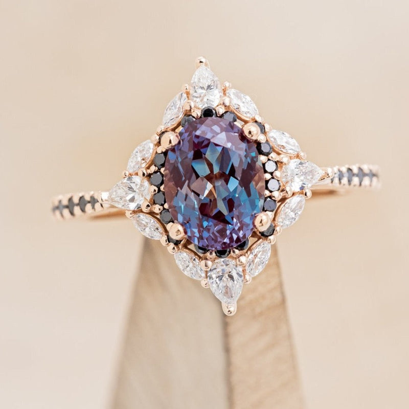 Shown here is "North Star", an oval lab-created alexandrite women's engagement ring with a diamond halo and black diamond accents, on stand front facing. Many other center stone options are available upon request.