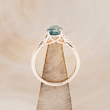 Shown here is "Roslyn", an oval moss agate women's engagement ring with diamond accents, side view on stand. Many other center stone options are available upon request.