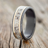 Shown here is "Hollis", a custom, handcrafted men's wedding ring featuring elk antler & 2 14K yellow gold inlays (1mm) on hammered, fire-treated black zirconium band, upright facing left. Additional inlay options are available upon request.
