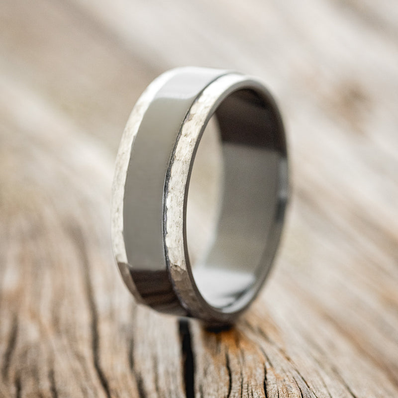 Shown here is "Sedona", a handcrafted men's wedding ring featuring a solid black zirconium band with hammered edges, upright facing left. The band was fire-treated before the edges were hammered causing the edges to be grey. 