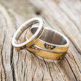 Shown here is "Golden", a matching wedding band set featuring buckeye burl with hand-panned Alaskan gold nugget inlays shown here set on titanium bands, upright facing left.