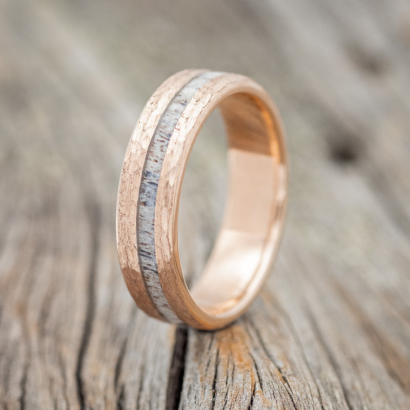 Shown here is "Vertigo", a custom, handcrafted hammered men's wedding ring featuring an offset antler inlay, shown here on a 14K gold wedding band, upright facing left. Additional inlay options are available upon request.