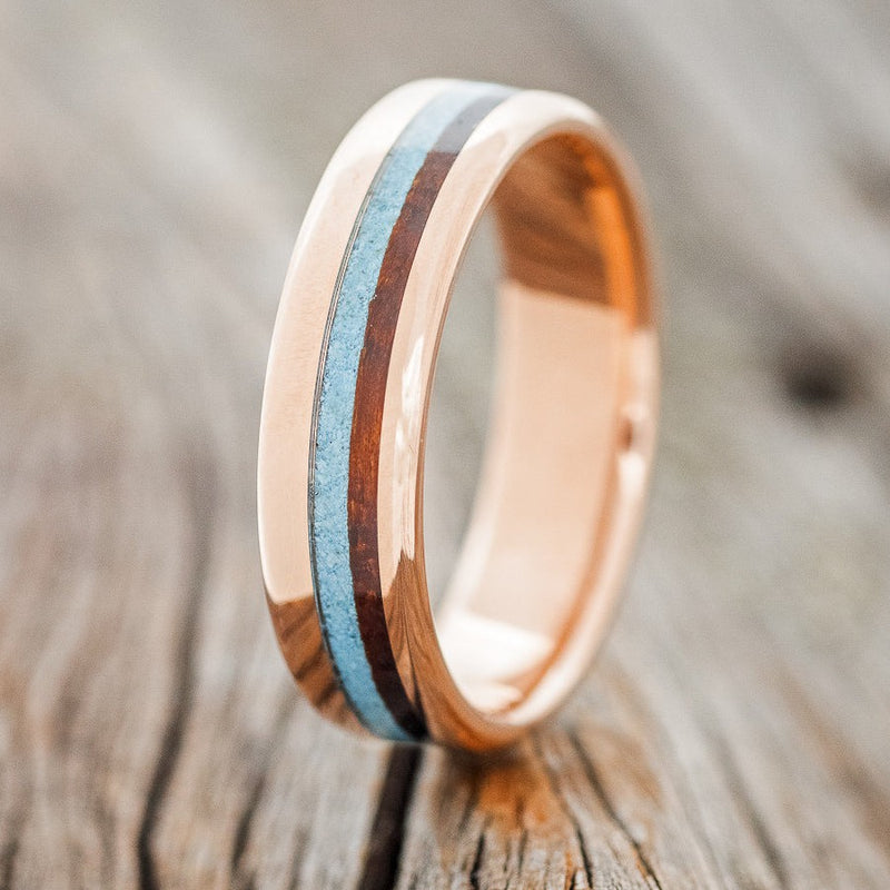 Shown here is "Castor", a custom, handcrafted men's wedding ring featuring an ironwood and turquoise inlay on a 14K gold band, upright facing left. Additional inlay options are available upon request.