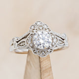 Shown here is "Eileen", a vintage-style moissanite women's engagement ring with a diamond halo, accents, and tracer, on stand front facing. Many other center stone options are available upon request. 