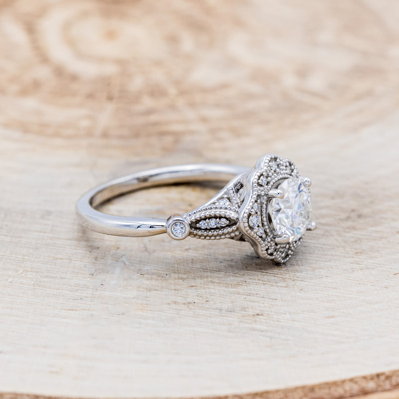 Shown here is "Eileen", a vintage-style moissanite women's engagement ring with a diamond halo, accents, facing right. Many other center stone options are available upon request.